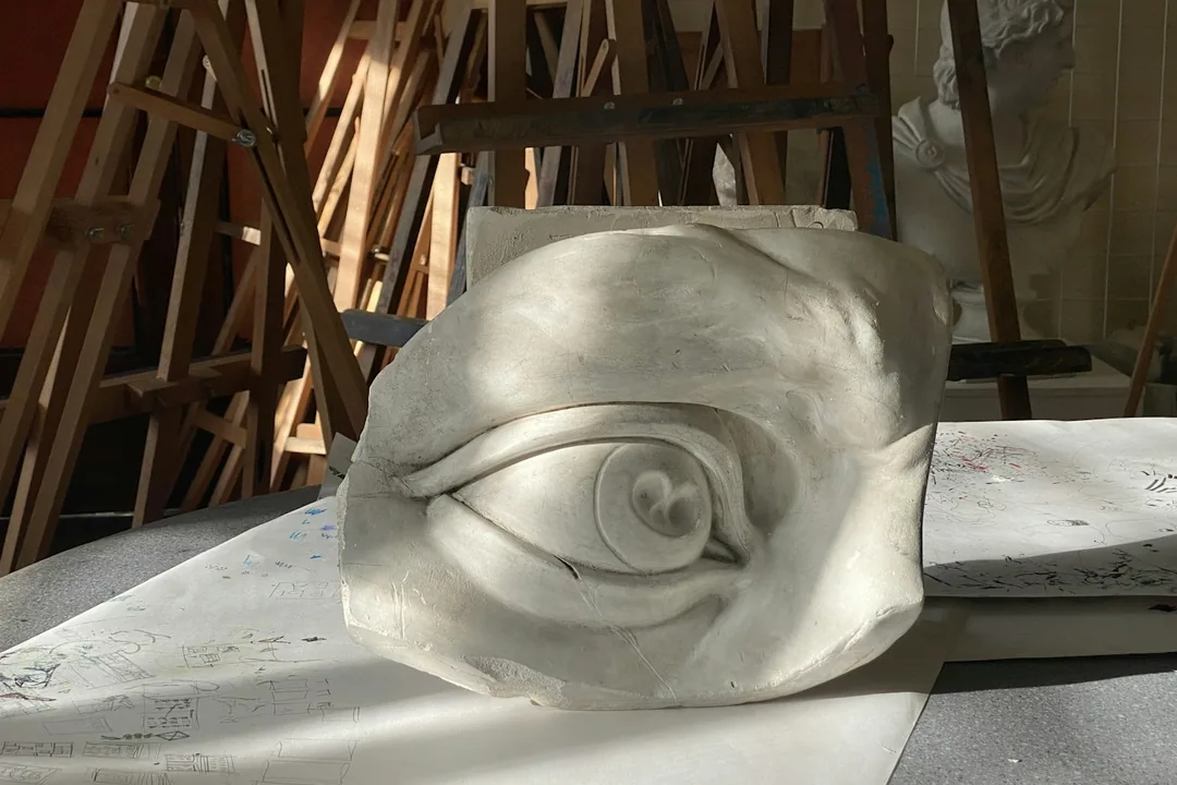 Vaciado en escayola de un ojo de gran tamaño apoyado sobre una mesa de taller, con caballetes de madera al fondo